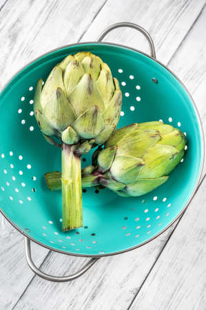 Two uncooked green artichokes in the colanderの写真素材