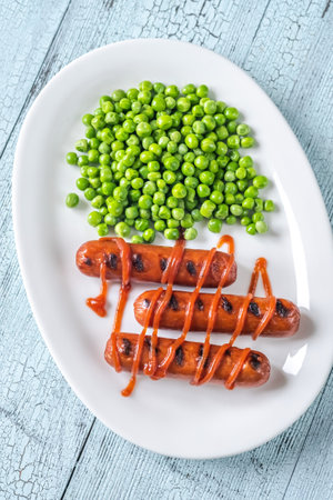 Grilled sausages with green peas on the plateの写真素材