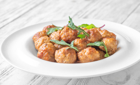 Tender chicken meatballs garnished with fresh rocket salad leaves.