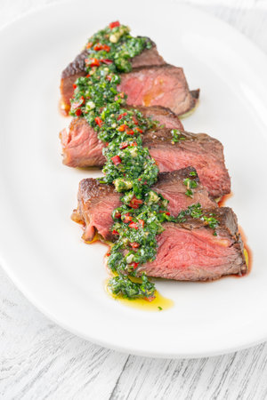 Portion of sliced strip steak with Chimichurri sauceの写真素材