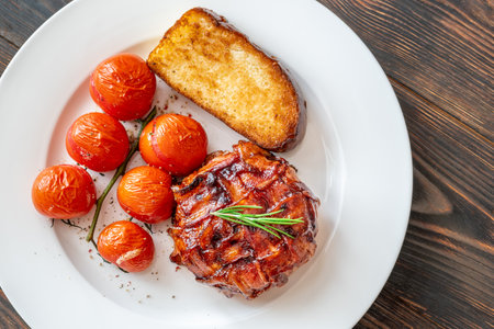 Bacon-wrapped food on a plate with roasted tomatoes and toasted bread.の写真素材