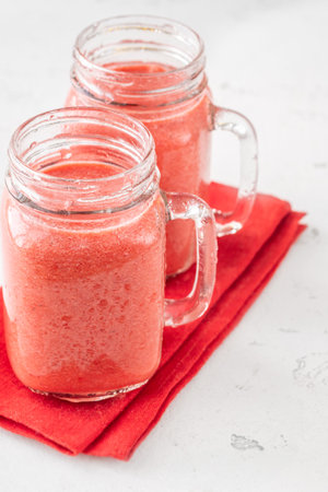 Creamy tropical smoothie with cherry, banana, and pineapple in mason jarsの写真素材