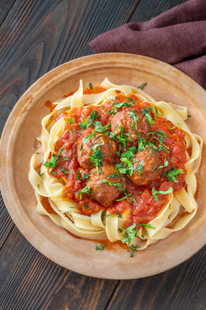 Tender meatballs in rich tomato sauce atop tagliatelle pasta, garnished with herbsの写真素材