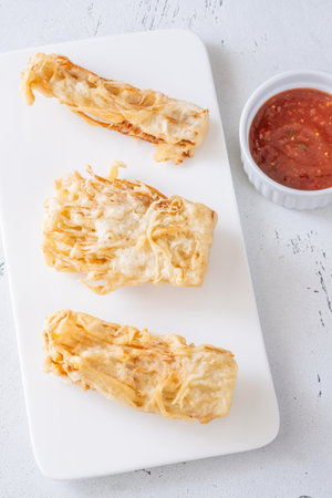 Golden enoki clusters deep-fried to crunch perfection beside sweet chili dipping bowlの写真素材