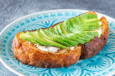 Bright avocado rests on creamy labneh, textures contrast beautifully on toasted breadの写真素材
