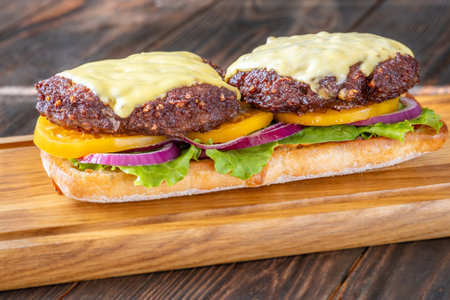 Layered sandwich with fresh ingredients stacked tall on rustic cutting board surfaceの写真素材