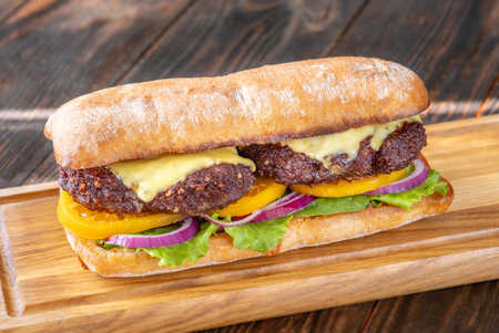Layered sandwich with fresh ingredients stacked tall on rustic cutting board surfaceの写真素材