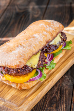 Layered sandwich with fresh ingredients stacked tall on rustic cutting board surfaceの写真素材