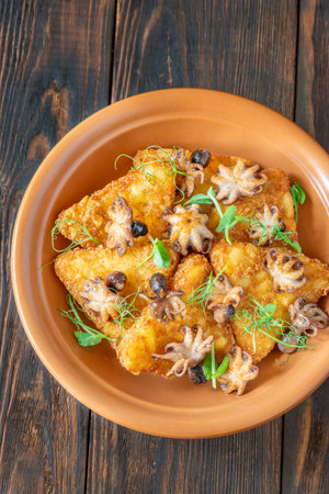 Crisp fritters and tender octopuses topped with greens on rustic wooden tableの写真素材