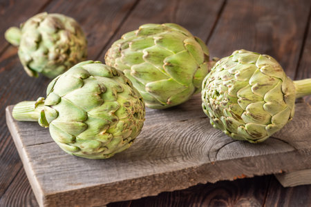 Whole raw artichokes with leafy texture resting on aged cutting board, rustic ambianceの写真素材