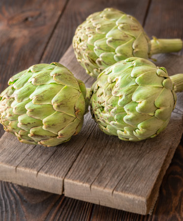 Whole raw artichokes with leafy texture resting on aged cutting board, rustic ambianceの写真素材