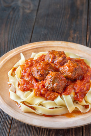 Tender meatballs in rich tomato sauce atop tagliatelle pasta, garnished with herbsの写真素材