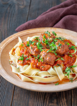 Tender meatballs in rich tomato sauce atop tagliatelle pasta, garnished with herbsの写真素材