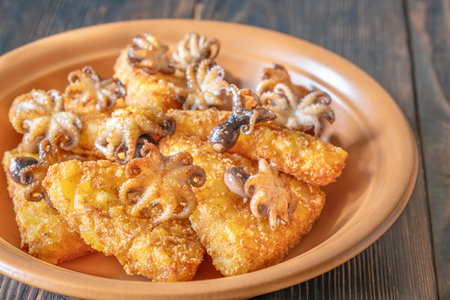 Crispy potato fritters paired with tender octopuses on weathered wood in daylightの写真素材