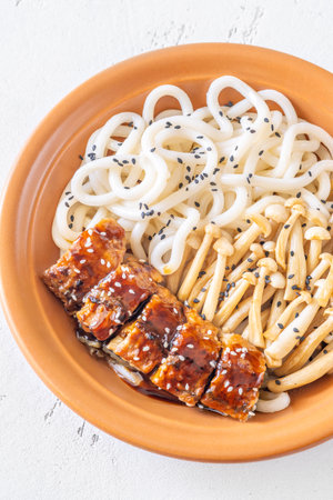 A hearty udon bowl topped with eel, mushrooms, and toasted sesame garnish
