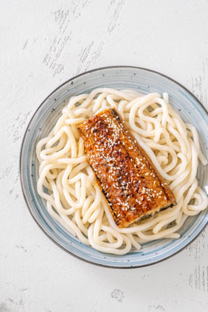 Thick udon noodles topped with glazed eel, richly coated in savory unagi sauceの写真素材