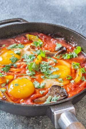 Eggs simmered in spiced tomato base with mushrooms, peppers, and fresh herbsの写真素材