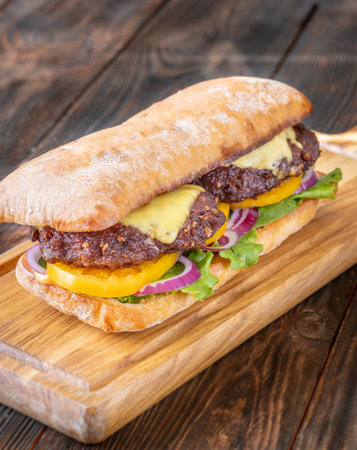 Layered sandwich with fresh ingredients stacked tall on rustic cutting board surfaceの写真素材