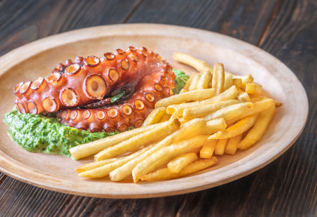 Roasted octopus tentacles served with creamy spinach and golden fries, rustic plating styleの写真素材