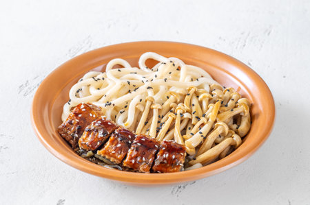 A hearty udon bowl topped with eel, mushrooms, and toasted sesame garnishの写真素材