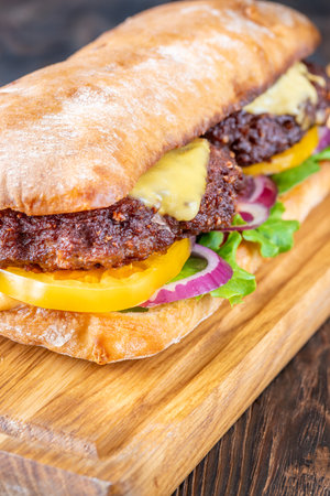 Layered sandwich with fresh ingredients stacked tall on rustic cutting board surfaceの写真素材