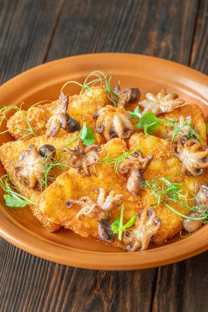 Crisp fritters and tender octopuses topped with greens on rustic wooden tableの写真素材