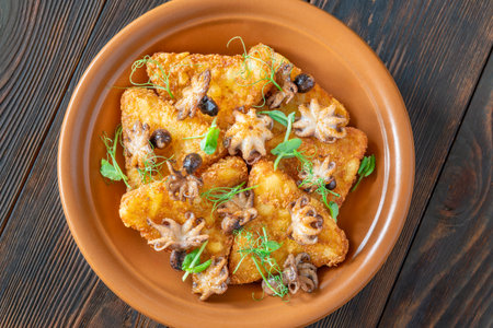 Crisp fritters and tender octopuses topped with greens on rustic wooden tableの写真素材