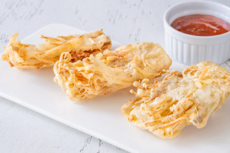 Golden enoki clusters deep-fried to crunch perfection beside sweet chili dipping bowlの写真素材