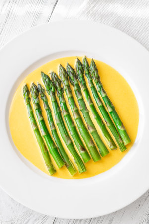 Steamed green asparagus resting atop rich Hollandaise, plated with minimal refined styleの写真素材