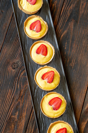 Row of golden mango tarts, each crowned with fresh strawberry, vibrant and delicateの写真素材