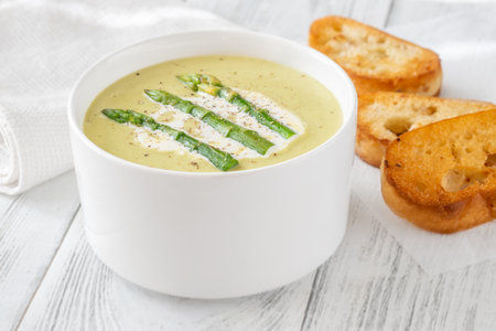 Velvety green soup topped with spears, cream swirl, and toasted breadの写真素材