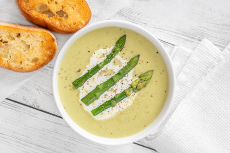 Velvety green soup topped with spears, cream swirl, and toasted breadの写真素材