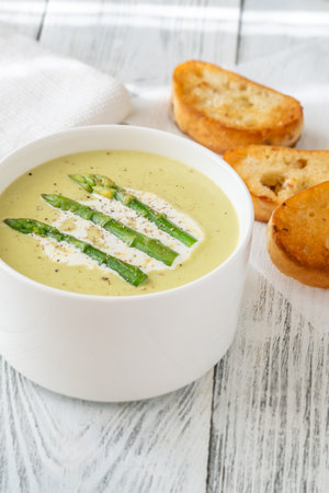 Velvety green soup topped with spears, cream swirl, and toasted breadの写真素材