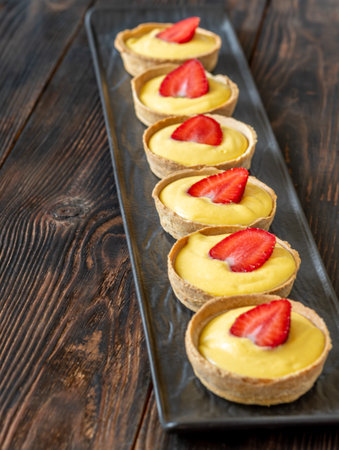 Row of golden mango tarts, each crowned with fresh strawberry, vibrant and delicateの写真素材