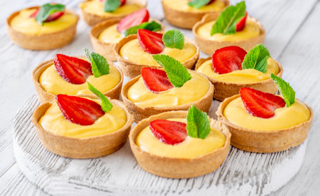 Golden mango tarts topped with strawberry slices and mint leaves, neatly arranged