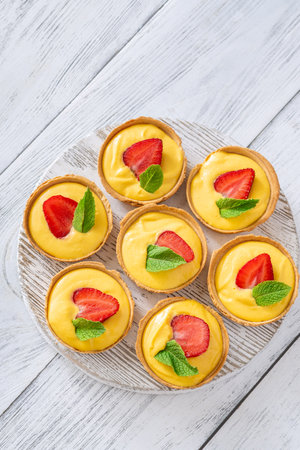 Golden mango tarts topped with strawberry slices and mint leaves, neatly arrangedの写真素材