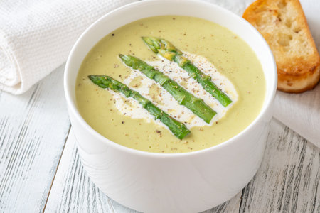 Velvety green soup topped with spears, cream swirl, and toasted breadの写真素材