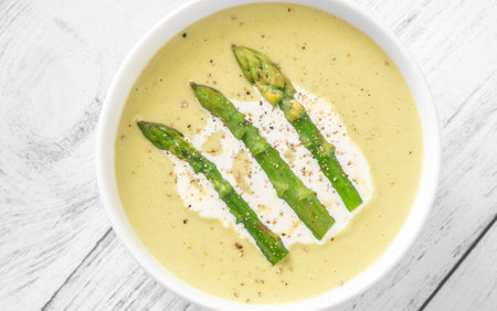 Velvety green soup topped with spears, cream swirl, and toasted breadの写真素材
