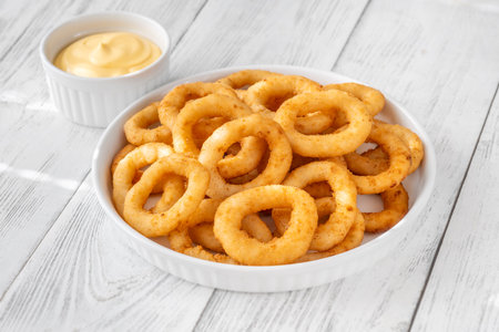 Battered onion rings paired with creamy cheese dip on rustic table settingの写真素材
