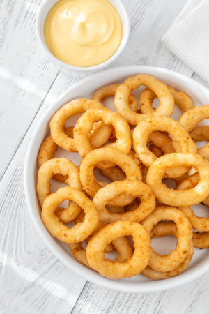 Battered onion rings paired with creamy cheese dip on rustic table settingの写真素材