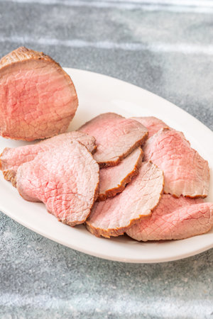 Pink centered beef with brown seared edges presented neatly on white plate
