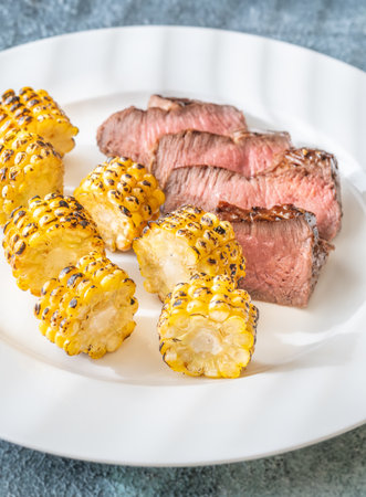 Tender beef slices and roasted corn segments served simply on white plateの写真素材