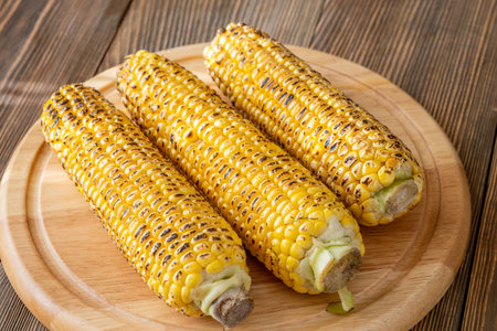 Vibrant yellow corn grilled until charred lightly placed on rustic cutting boardの写真素材