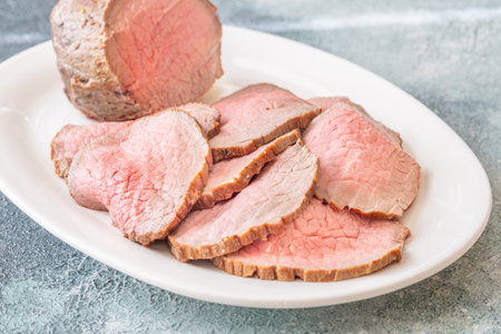 Pink centered beef with brown seared edges presented neatly on white plateの写真素材
