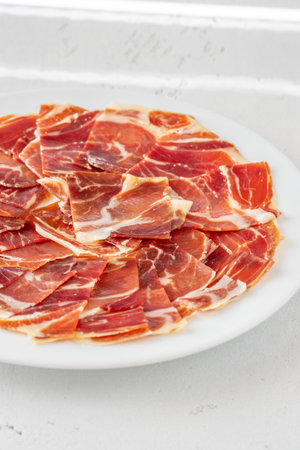 Cured Spanish ham slices fan out delicately across clean, white ceramic round plate