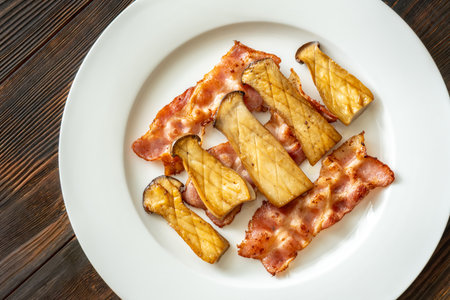 Savory eryngii mushrooms paired with crisp bacon, plated simply for indulgent flavorの写真素材