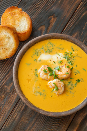 Shrimp bisque in rustic clay bowl, served alongside toasted golden baguette slicesの写真素材