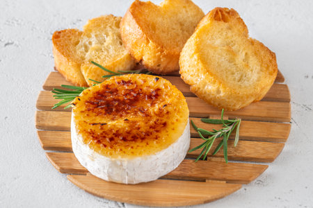 Warm soft cheese topped with sugar crust, served with rosemary sprigs and baguette slicesの写真素材