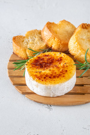 Warm soft cheese topped with sugar crust, served with rosemary sprigs and baguette slicesの写真素材