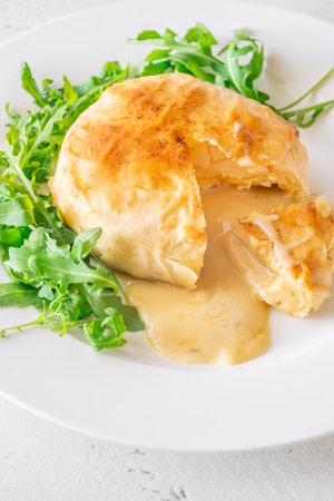 Soft molten cheese flows from pastry crust beside cranberry sauce and fresh arugula greensの写真素材